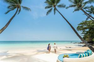 a couple walking on a beach with palm trees at Four Seasons Resort Koh Samui - SHA Extra Plus in Mae Nam