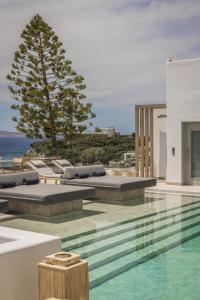 a pool with lounge chairs and a tree on a building at Grace Mykonos in Agios Stefanos