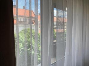 - une fenêtre avec des rideaux blancs et une vue sur un bâtiment dans l'établissement N-Apartman Central, à Mosonmagyaróvár