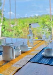 uma mesa com uma garrafa de água, copos e pires em Atulya Lake View - Resort and Spa em Mirissa