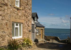 a stone building with the ocean in the background at Harbour Masters House in Craster