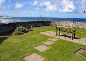 un banco del parque sentado en el césped cerca del océano en Bluegrass en Seahouses