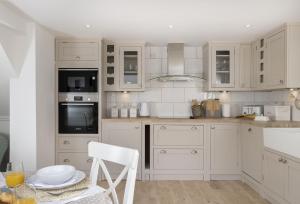 a kitchen with white cabinets and a table with a chair at Winacres Cottage in Nailsworth