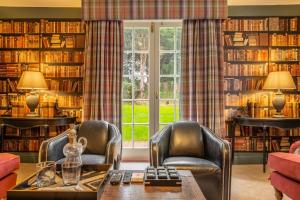 a library with two chairs and a table in front of a window at The Farmhouse, Nether Hall Estate in Pakenham