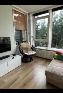 sala de estar con TV, silla y ventanas en Apartment Mellow Stay Amsterdam, en Ámsterdam