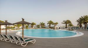 uma piscina num resort com cadeiras e palmeiras em ILUNION Costa Sal Lanzarote em Puerto del Carmen