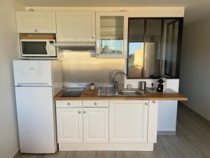 a white kitchen with a sink and a refrigerator at Appartement pieds dans l’eau Vue Mer Bormes Les Mimosas in Bormes-les-Mimosas