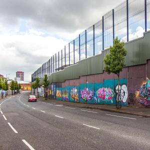 um carro a descer uma rua ao lado de um edifício com graffiti em The Lucky Oak em Belfast