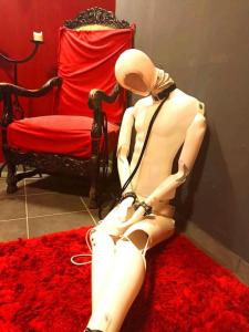 a mannequin sitting on a red rug next to a chair at Budapest BDSM Studio in Budapest