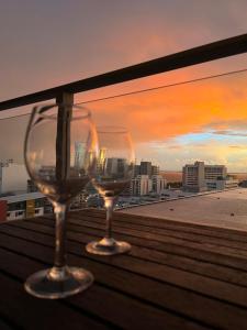 two wine glasses sitting on a balcony with a sunset at Darwin City Suites with Harbour View in Darwin