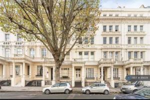 Deux voitures garées devant un grand bâtiment blanc dans l'établissement [Hyde park-Notting Hill] London Studio Apartment, à Londres