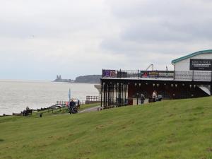 a pier with people sitting on the grass near the water at Barons Mews in Herne Bay