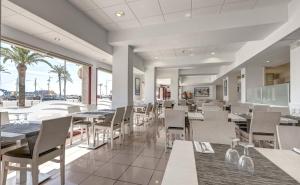 un restaurante con mesas y sillas blancas y palmeras en Rosamar Maritim 4*, en Lloret de Mar