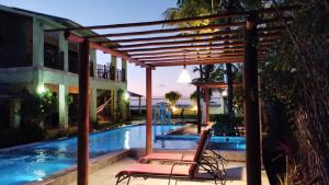 a pair of chairs sitting under a pergola near a swimming pool at Pousada Chantilly in São Miguel do Gostoso