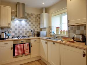 una cucina con armadi bianchi e piano cottura di Kestrel Cottage - 27937 a Cambusbarron