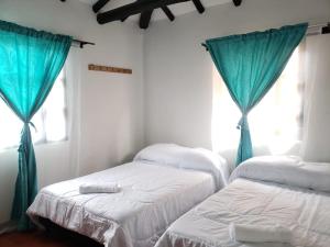 two beds in a room with blue curtains at Casa Villa Ramos in Villa de Leyva