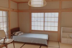 1 dormitorio con 1 cama, 1 silla y ventanas en 一番館※温泉街に近く、心が落ち着く別荘地同樺順荘 en Kusatsu