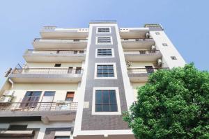 ein hohes weißes Gebäude mit einem Baum davor in der Unterkunft Collection O 81235 Hotel Aashiyana in Neu-Delhi