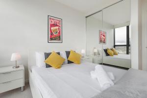 a white bedroom with a large bed with yellow pillows at KULA Docklands in Melbourne