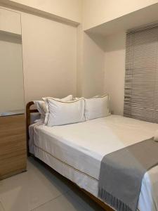 Schlafzimmer mit einem Bett mit weißer Bettwäsche und Kissen in der Unterkunft Alexa at Tanglin Apartemen in Surabaya
