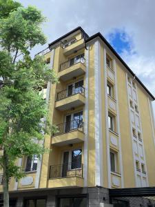 un edificio alto de color amarillo con balcones y un árbol en COOP Apartments, Sofia, en Sofía