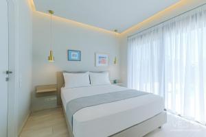 a white bedroom with a bed and a large window at Olive Grove Suites - Villas with private pool and garden in Nikiti