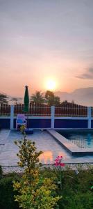 a pool with a table and a umbrella and the sunset at Poonsap Homestay in Nan