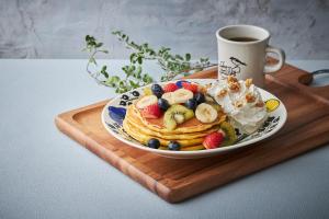 a plate of pancakes with fruit and whipped cream and a cup of coffee at Via Inn Prime Osaka Kyobashi in Osaka