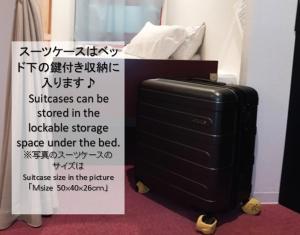 un panneau à côté d'une valise à côté d'un lit dans l'établissement セルフチェックイン Guest House SHUKUGO UTSUNOMIYA, à Utsunomiya