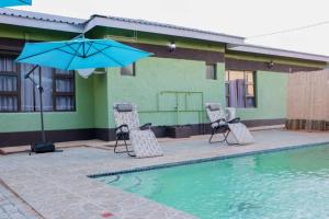 ein Paar Stühle und ein Regenschirm neben einem Pool in der Unterkunft Amariah Lodge in Kasane