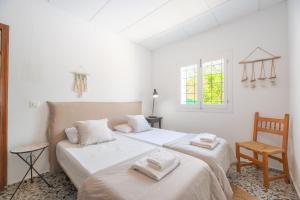 Un dormitorio blanco con 2 camas y una silla en Casa Can Vert con piscina en Santa Gertrudis de Fruitera