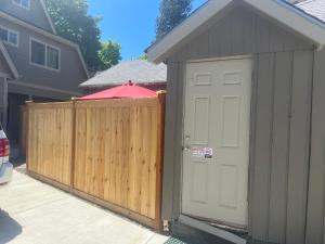 a shed with a white door next to a fence at NEW! Unique Coeur d’Alene Cottage. 1/2 Mi to Dtwn in Coeur d'Alene