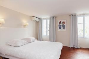 a bedroom with a white bed and two windows at Coq Hotel in Cogolin