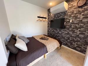 さいたま市にあるおもてなしハウスさいたまのレンガの壁にテレビとベッドが備わるベッドルーム1室が備わります。