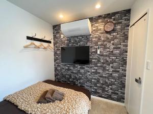 um quarto com uma parede de tijolos, uma cama e uma televisão em おもてなしハウスさいたま em Saitama