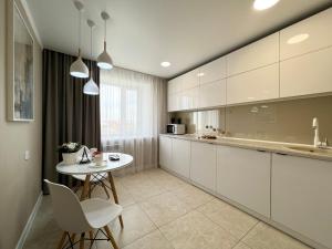 uma cozinha com armários brancos e uma mesa e cadeiras em Luxury apartments em Pavlodar
