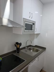a white kitchen with a sink and a microwave at Lyrioshomes Apartamento Filpo Rojas , Sevilla in Seville