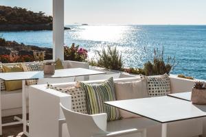 a patio with white tables and chairs and the ocean at Apollo Resort in Agia Marina Aegina