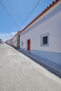 a white building with a red door next to a street at Rustic & Aesthetic House in Alqueva with Pool in Granja