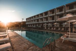 a hotel swimming pool with chairs and the sun setting at Apollo Resort in Agia Marina Aegina