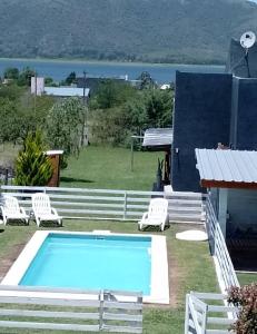 a pool with white chairs and a house at Cabañas Espinillos del Lago in Potrero de Garay