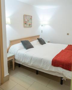 1 dormitorio con cama blanca y manta roja en Apartamentos Oasis Sol, en Maspalomas