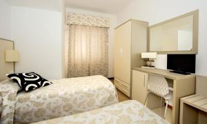a hotel room with two beds and a desk and a television at Hotel Lucerna in Castiglione della Pescaia