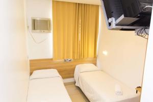 a small room with two beds and a tv at Minuano Hotel Home próximo ao aeroporto in Porto Alegre