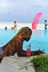 Eine Frau im Bikini, die mit einem Drink am Strand liegt. in der Unterkunft NDAME Paje Hotel in Paje