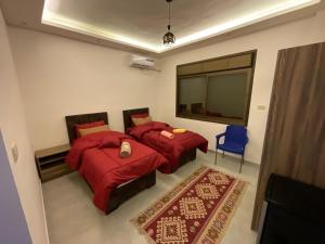 a bedroom with two beds with red comforters and a blue chair at Black IRIS in Jerash