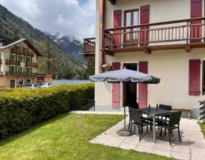 une table et des chaises avec un parasol en face d'un bâtiment dans l'établissement Charmant 2,5 pièces avec jardin à 2 pas du lac, à Champex-Lac