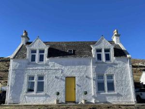 una casa blanca con puerta amarilla en Todday Snug Self Catering Studio, en Ersary