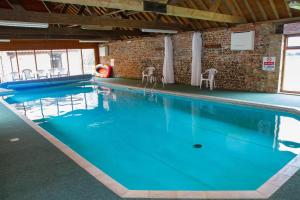 a large swimming pool with blue water in a building at Great Barn in Colkirk