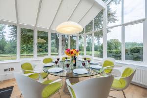 a conservatory dining room with a glass table and white chairs at Beech House in Little Walsingham